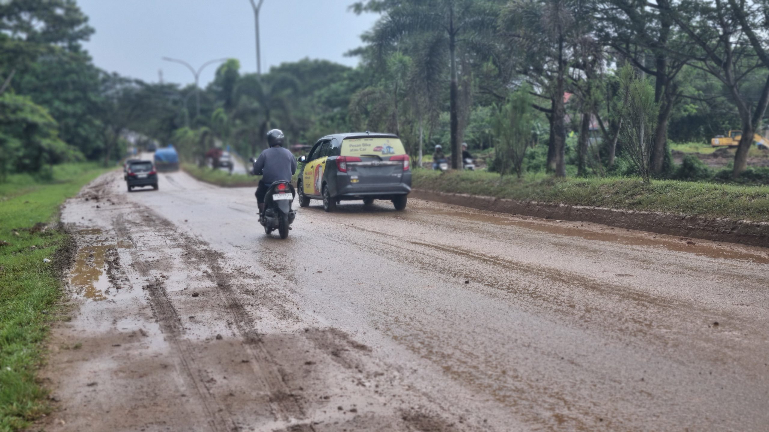 Alt text: Kondisi jalan di Kilometer 16, Kota Sorong, tampak berlumpur dan licin akibat tumpahan tanah dari truk proyek pembangunan gedung pemerintahan. Seorang pengendara motor terlihat berhati-hati melintasi jalan yang kotor dan berbahaya.